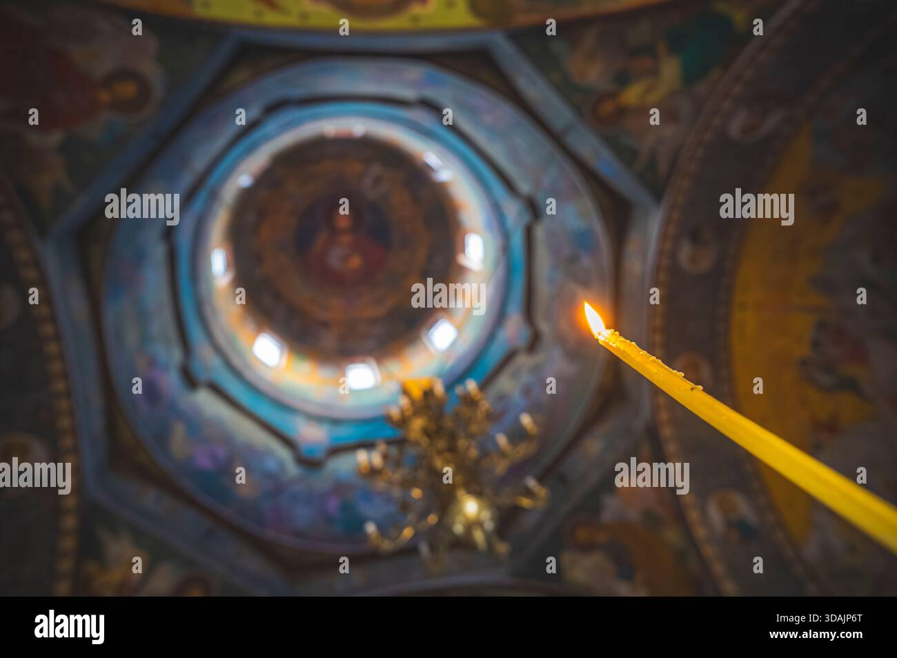 Petrosani, Roumanie 22 novembre 2025 : bougie de prière allumée flamboyante éclatante contrastant avec le dôme de plafond peint orné d'une église orthodoxe Banque D'Images