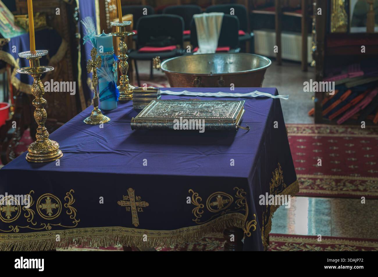 Petroșani, Roumanie, 22 novembre 2025 : table avec une broderie de croix en tissu violet, livre gospel à reliure argentée et chandeliers dorés dans une église Banque D'Images