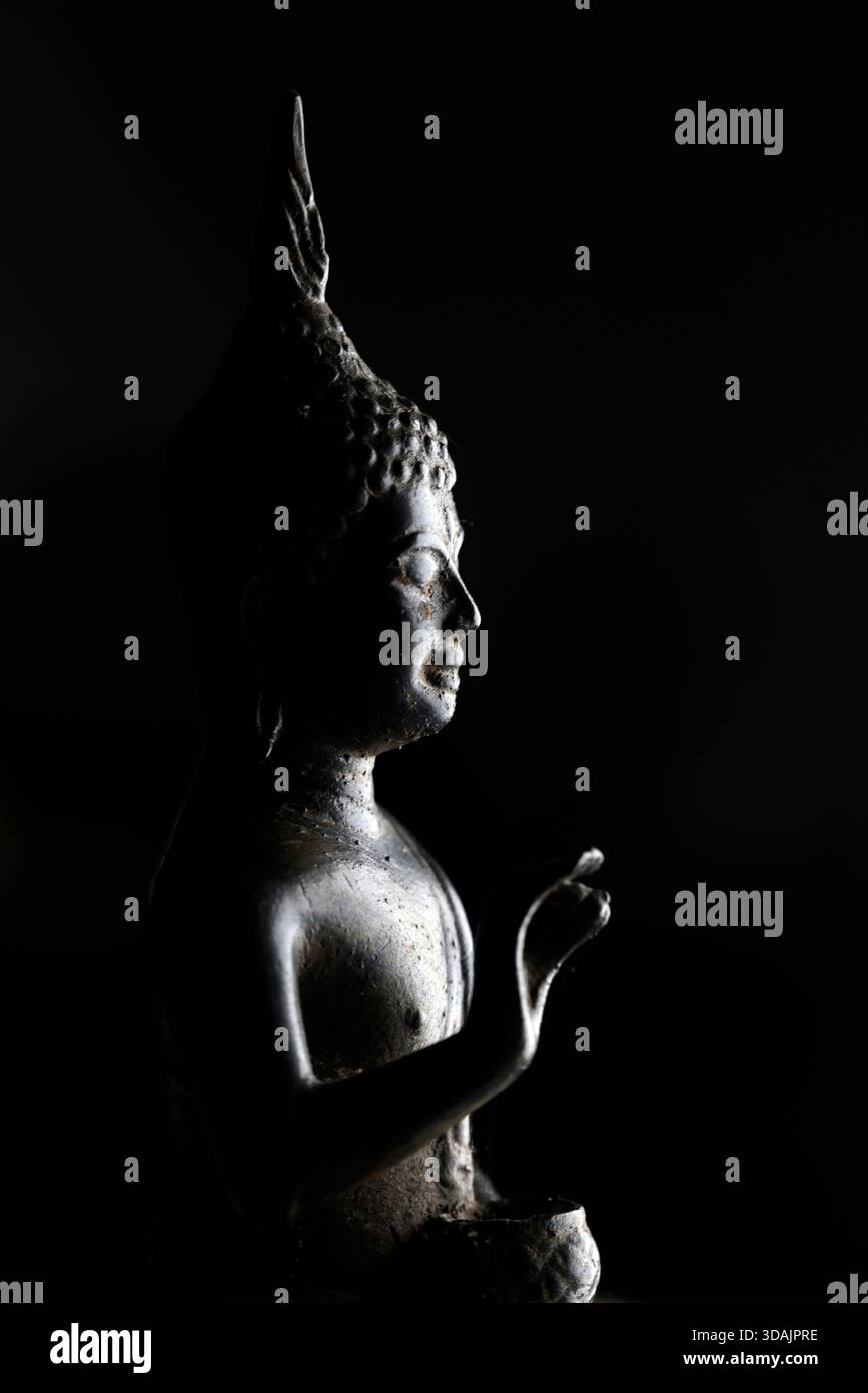 Figure de Bouddha asiatique assise gracieusement, offrant bénédiction et paix, capturée sous un éclairage dramatique, fond minimaliste. Banque D'Images