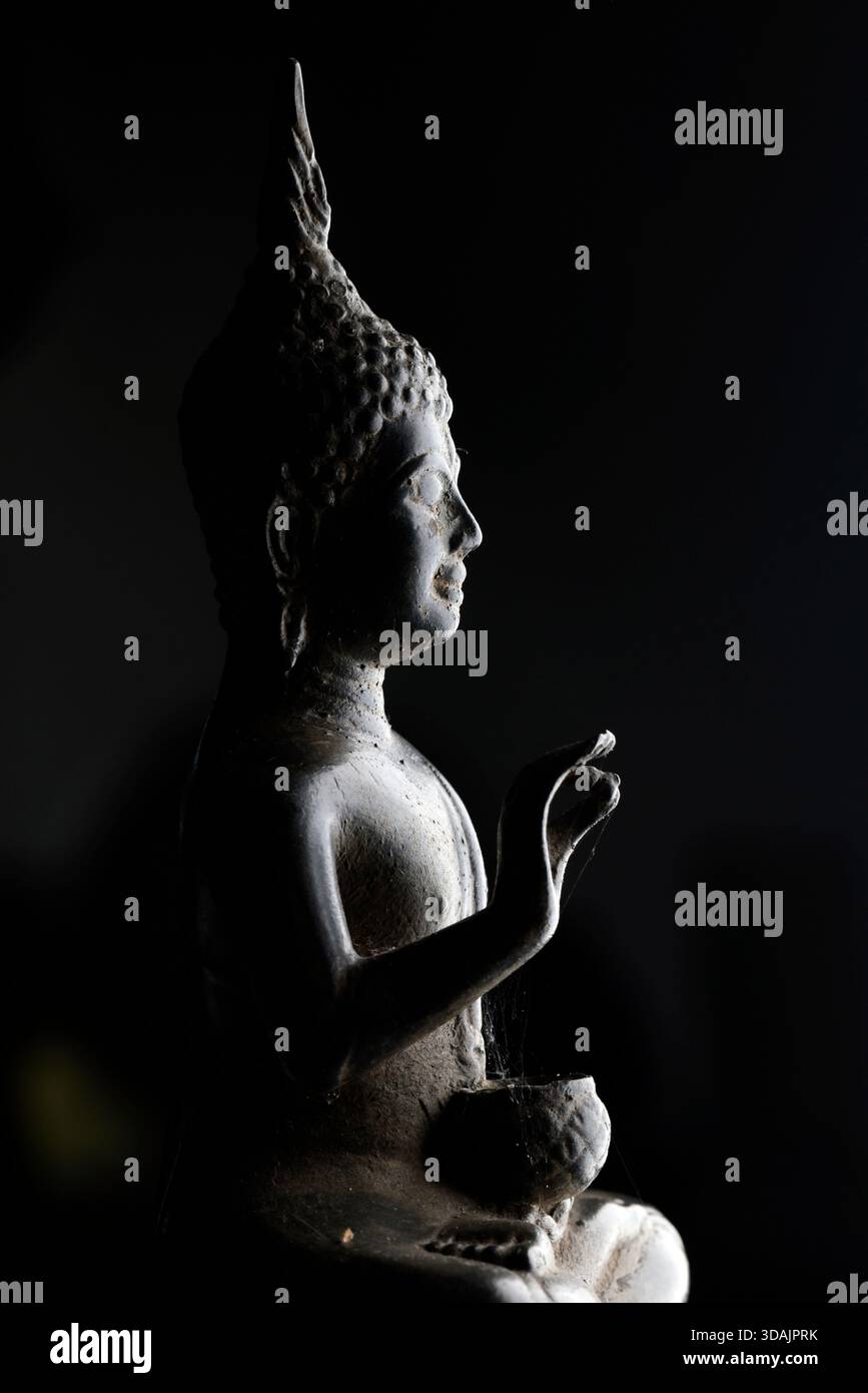 Figure de Bouddha asiatique assise gracieusement, offrant bénédiction et paix, capturée sous un éclairage dramatique, fond minimaliste. Banque D'Images