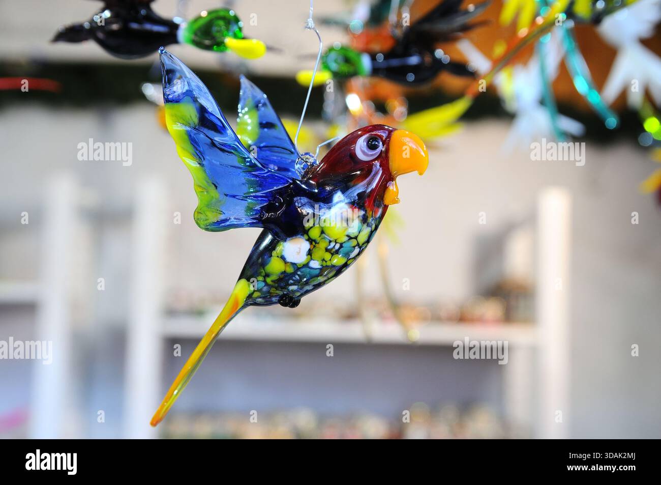 Gros plan d'un ornement d'oiseau en verre coloré suspendu à un marché de Noël. Fond flou avec des décorations festives de stalle. Banque D'Images