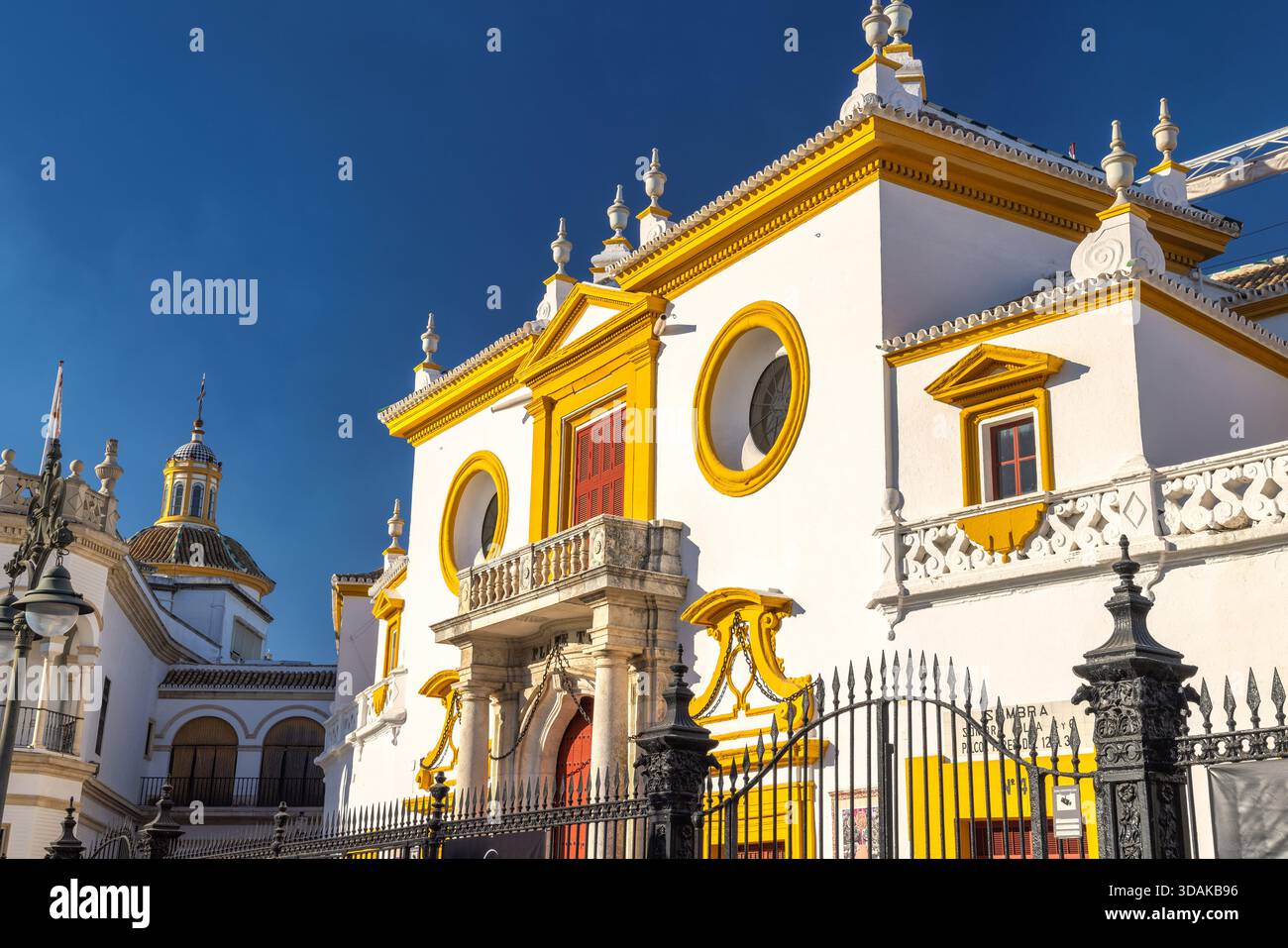 Séville, Espagne - 8 septembre 2024 : bâtiment blanc avec garniture jaune, détails ornés et une porte rouge. Les détails architecturaux sont proéminents sous un clair Banque D'Images