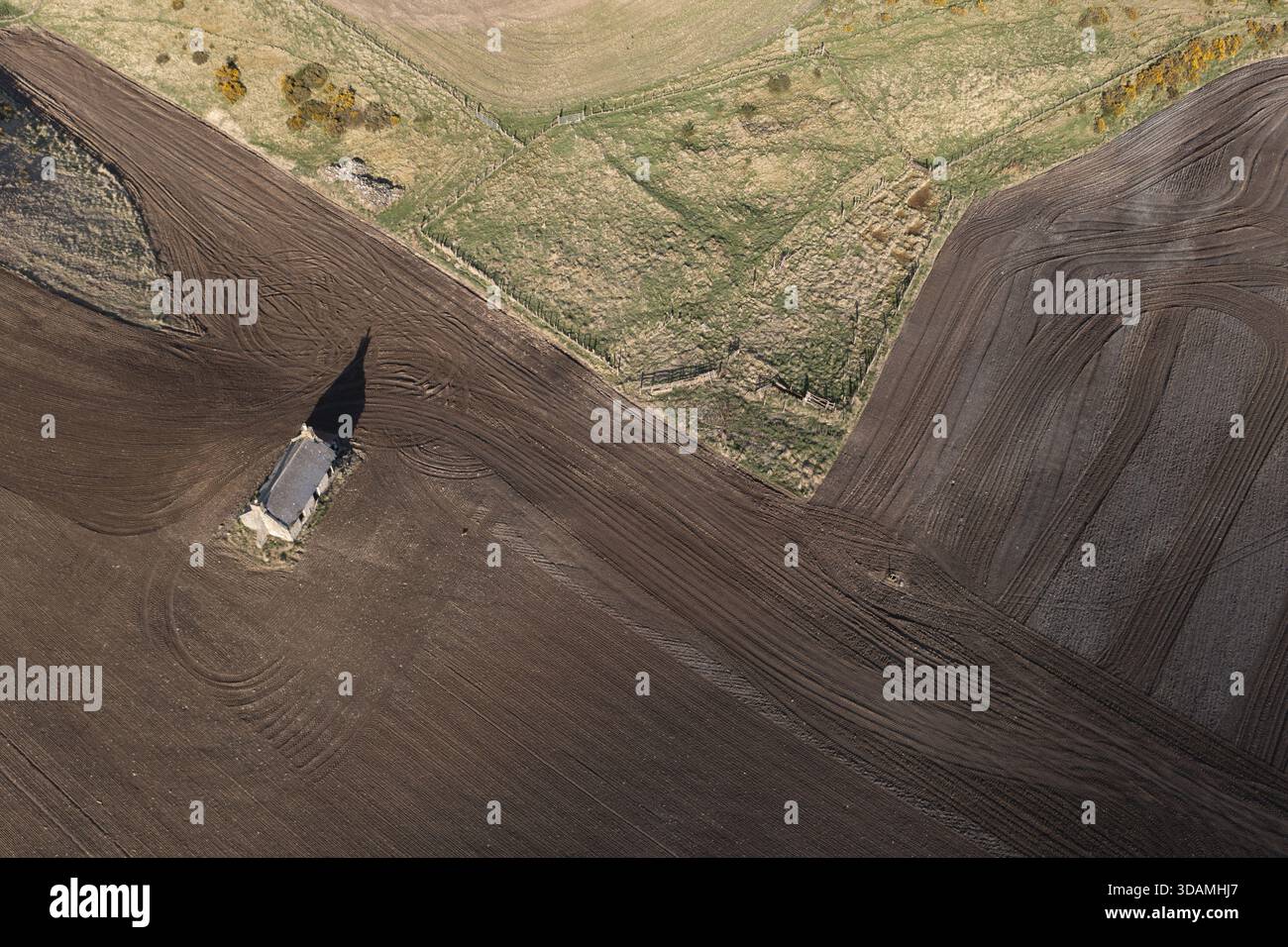 Vue aérienne d'un bâtiment solitaire projetant une longue ombre à travers la terre fraîchement labourée et sombre rencontrant les champs verdoyants dans un patchwork de beaux paysages ruraux Banque D'Images