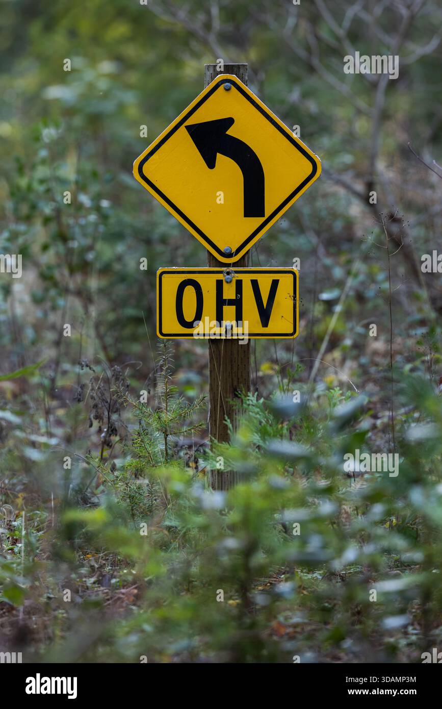Un plan précis d'un panneau d'avertissement jaune en forme de losange indiquant une courbe à gauche nette, jumelé à une plaque secondaire désignant la zone pour le VHO (Off-Highwa Banque D'Images