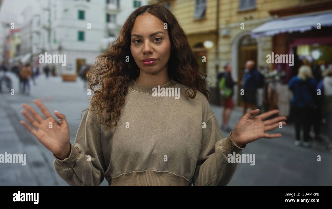 Jeune femme afro-américaine debout avec les paumes levées sur la rue animée de la ville, les mains ouvertes vers la caméra, expression neutre ; confiance tranquille. Banque D'Images