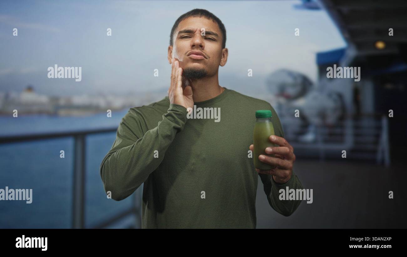 Homme tenant la bouteille de jus vert touche la joue avec les yeux fermés sur la jetée de la rue près de l'eau et de la balustrade ; dégoût. Banque D'Images