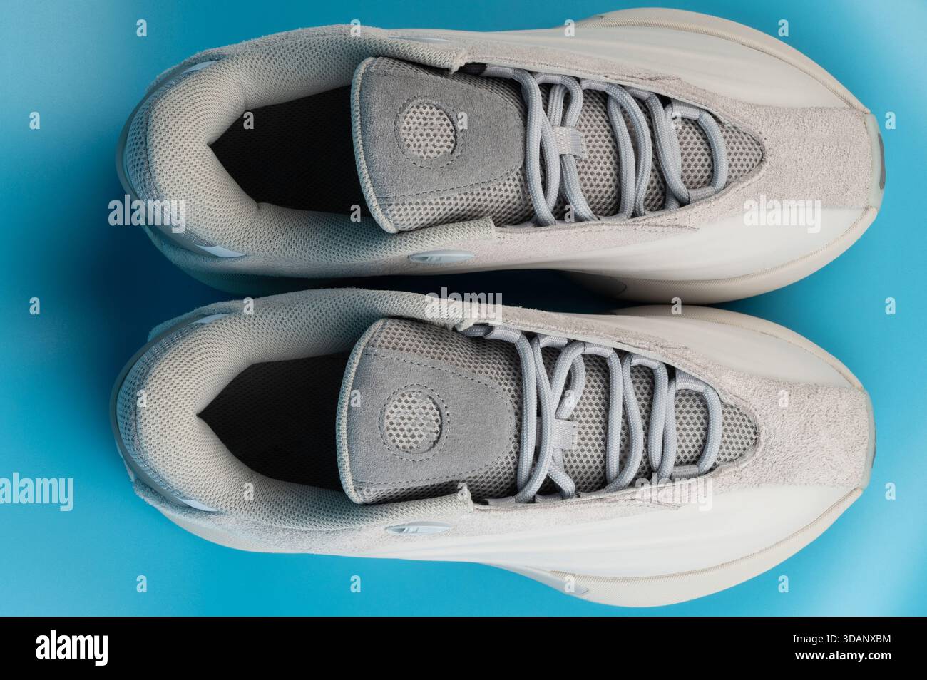 Paire de sneakers repose sur une surface bleue lisse sous une lumière douce, montrant des détails comme des lacets et des matériaux. Banque D'Images