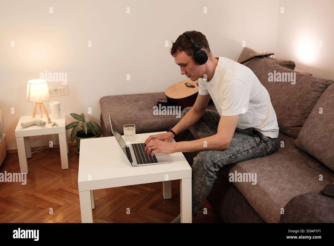 Un homme travaille sur son ordinateur portable tout en étant assis sur le canapé. Le concept reflète la productivité et le travail à distance dans un environnement domestique détendu. Banque D'Images