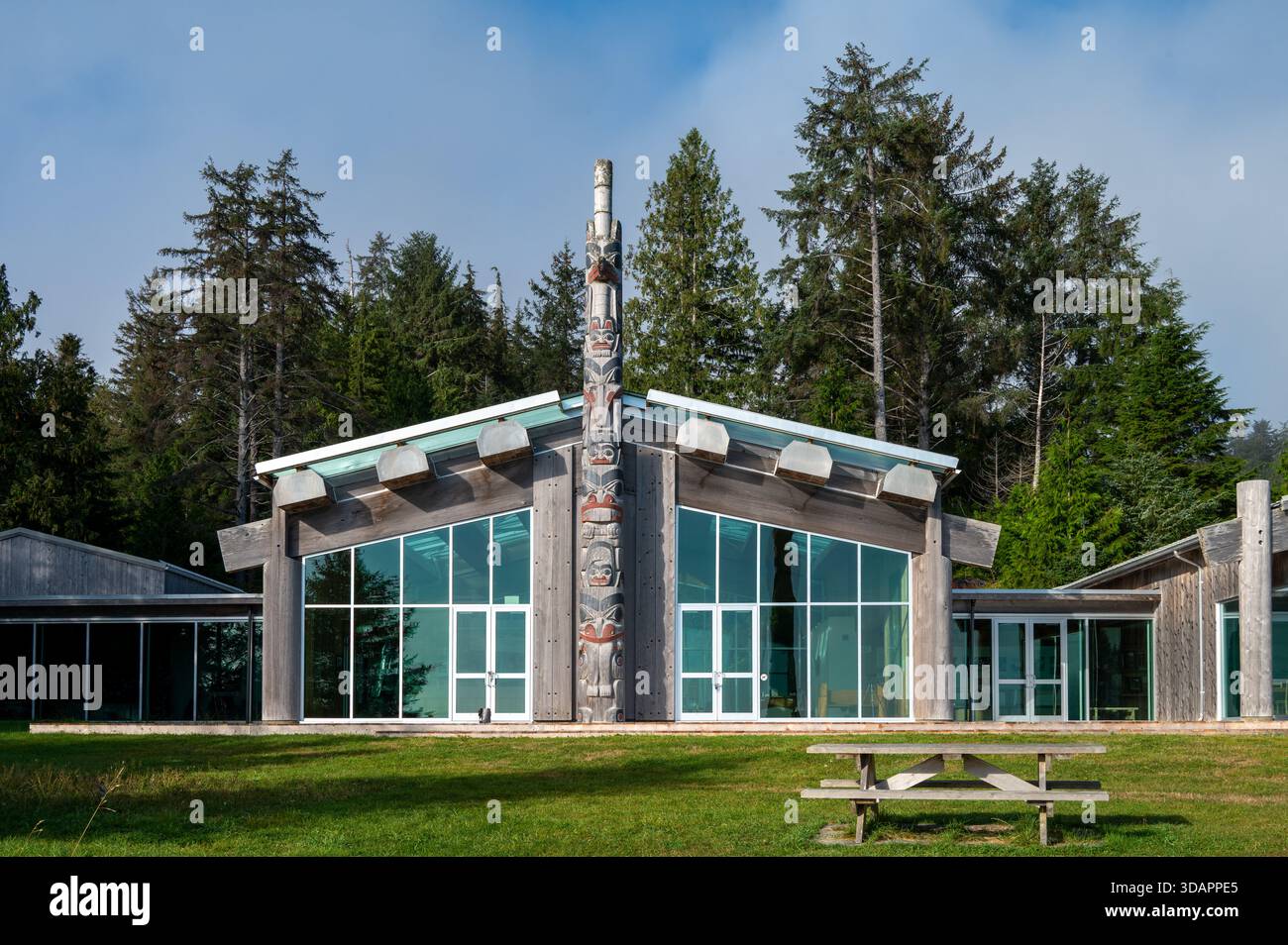 Le Centre du patrimoine haïda à Kay Llnagaay à Skidegate, avec un poteau de monument sculpté et le bâtiment principal en cèdre avec un fond de forêt. Banque D'Images