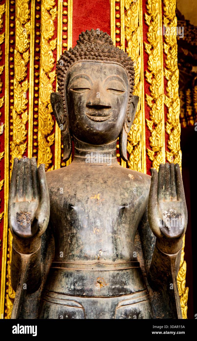 Ancienne statue de Bouddha en bronze avec les mains levées, fond orné. Banque D'Images