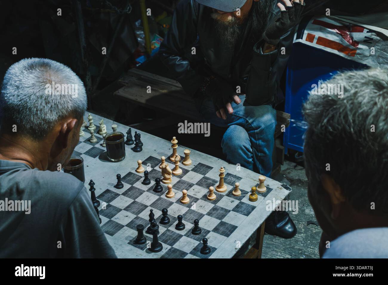 Balikpapan, Indonésie - 1er novembre 2025. Vue de haut en bas montrant une concentration intense pendant une partie sérieuse d'échecs de rue entre des hommes locaux la nuit. Banque D'Images