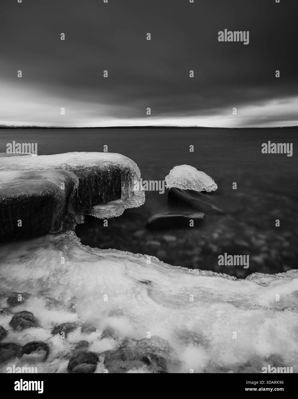La glace recouvre les rochers au bord du lac Femunden en Norvège. L'eau est sombre et le ciel nuageux. Cette scène capture l'atmosphère froide de WINT Banque D'Images
