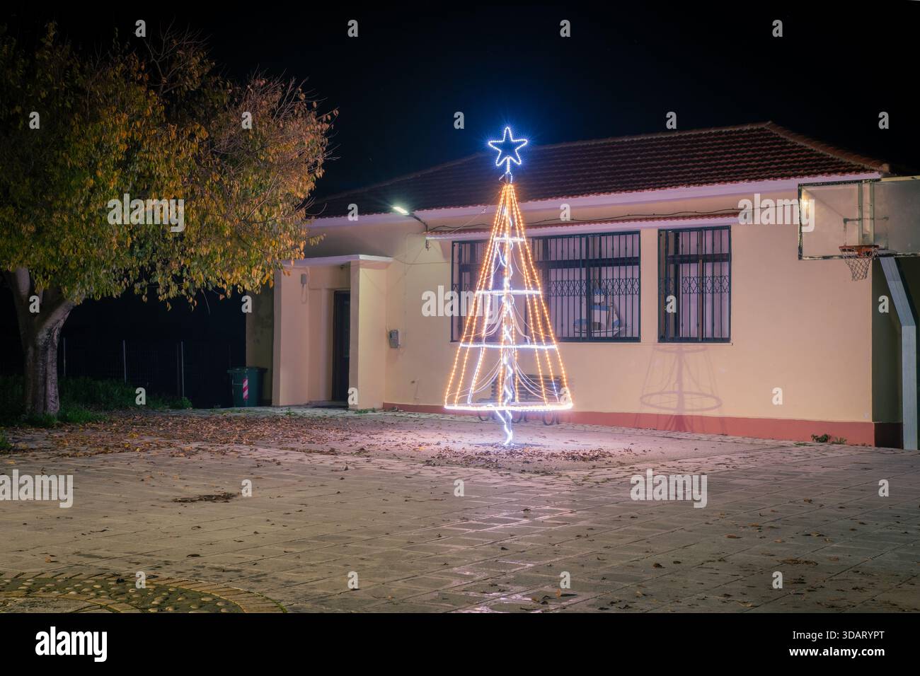 Installation lumineuse extérieure d'arbre de Noël la nuit dans un petit village ou une place de ville avec un bâtiment traditionnel en arrière-plan. Fête ce Banque D'Images