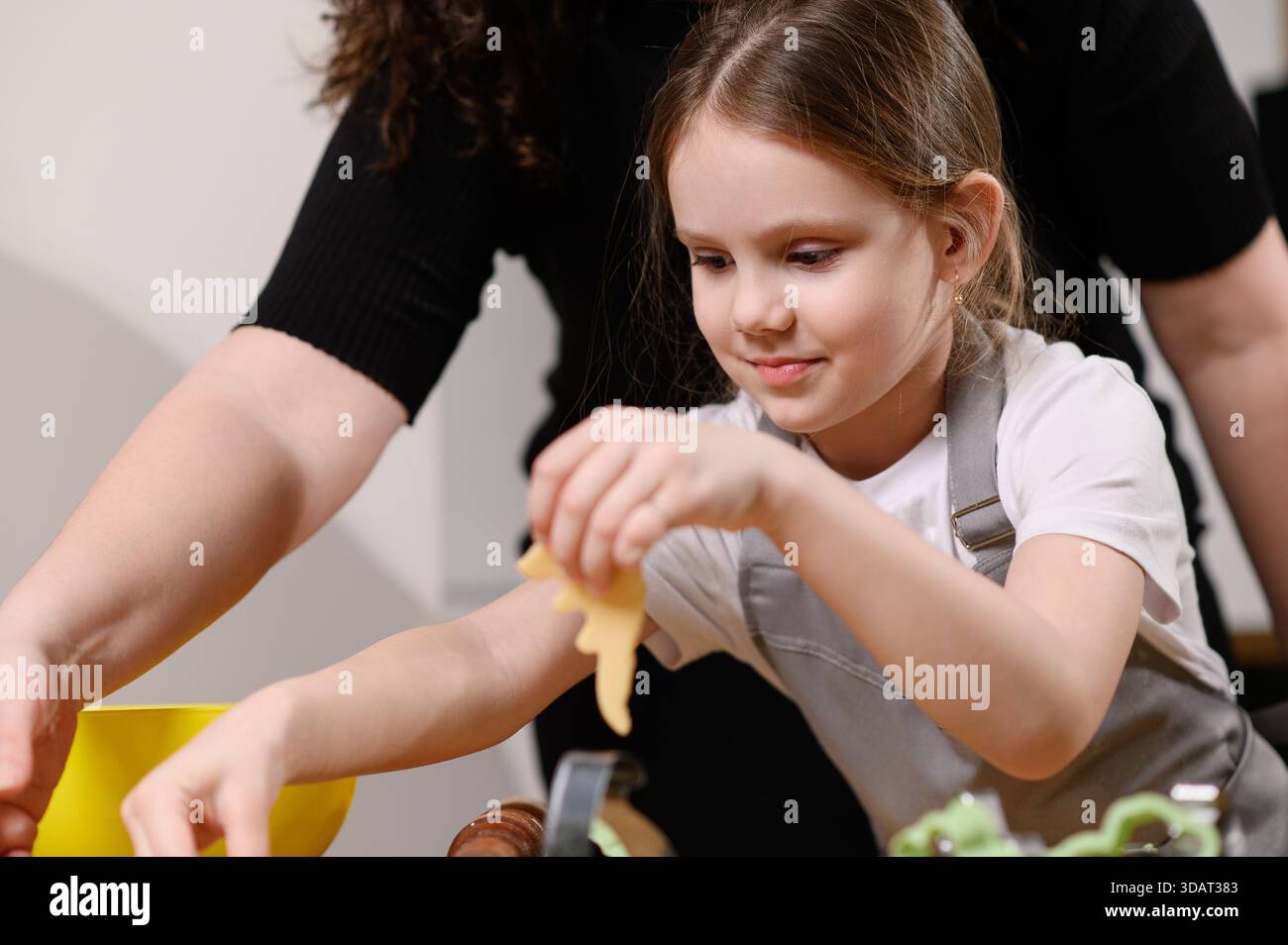 L'enfant et la mère découpent les biscuits de la pâte et les déposent sur une plaque à pâtisserie. Préparation de desserts familiaux. Banque D'Images