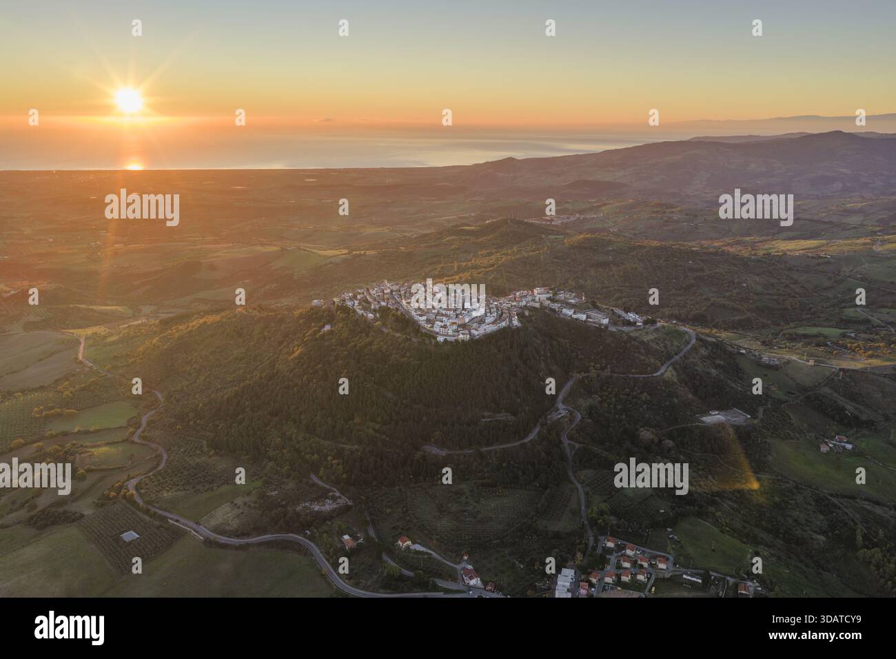 Vue aérienne d'une ville perchée dans la lueur chaude du soleil couchant, avec la mer reflétant la lumière dorée, Rotondella, Basilicate, Italie. Banque D'Images