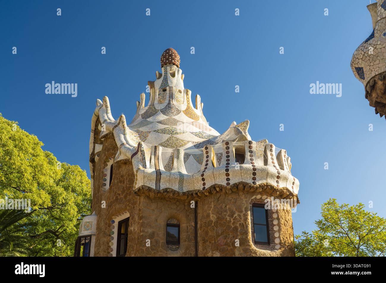 Vue sur des bâtiments fantaisistes recouverts de mosaïque aux toits coniques s'élevant contre un ciel bleu éclatant, encadré par des arbres verdoyants, créant une scène de conte de fées, P Banque D'Images