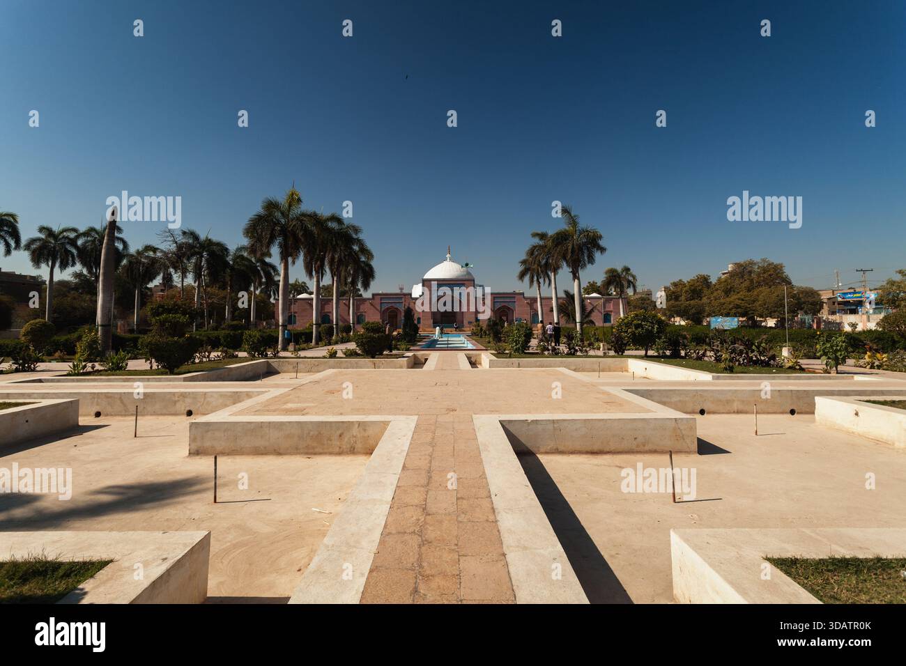 Vue de la façade rose de la mosquée Shah Jahan et des dômes blancs s'élevant au-delà du jardin symétrique, illuminé par le ciel clair, Thatta, Sindh, Pakista Banque D'Images
