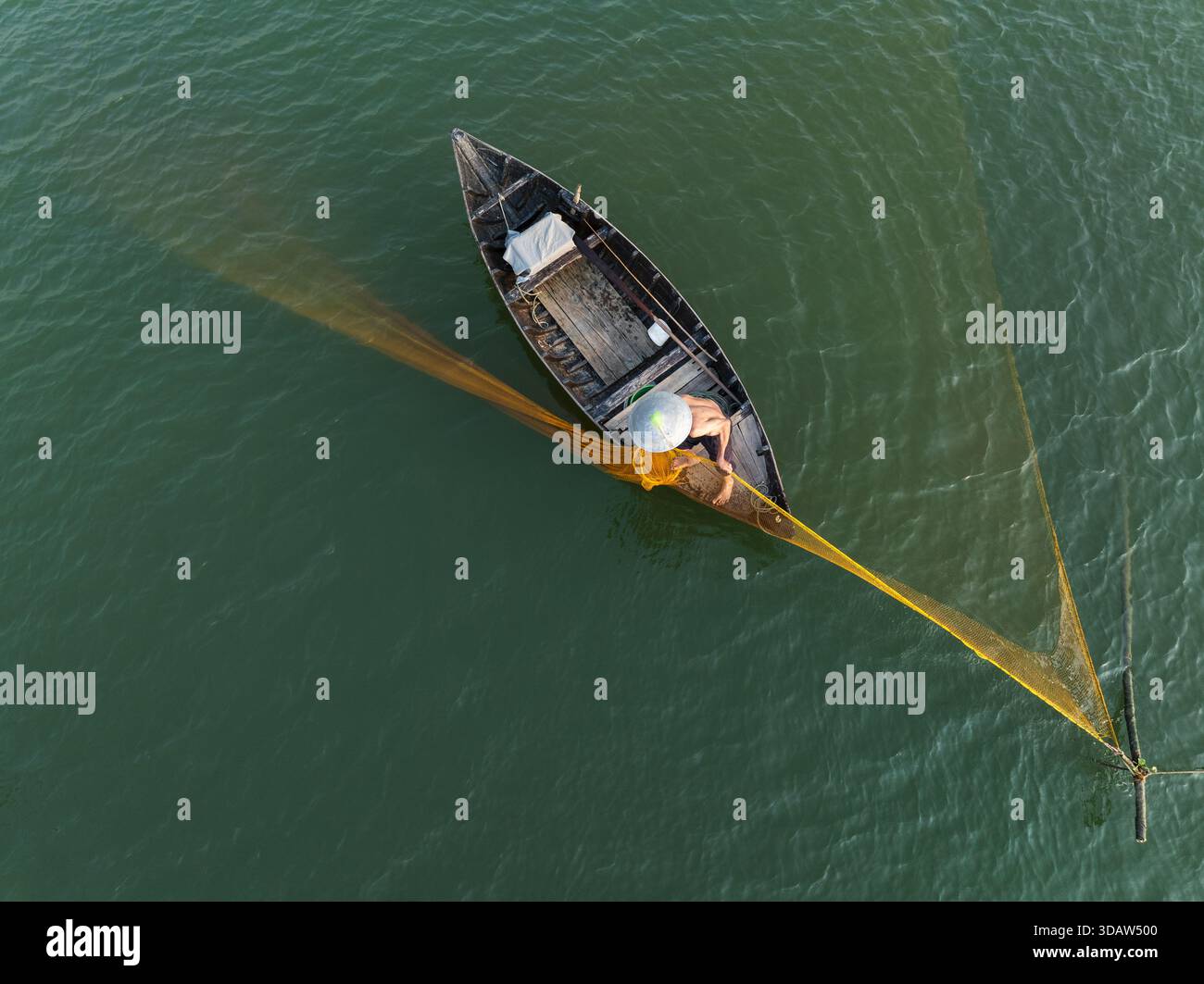 Vue aérienne d'un pêcheur solitaire jette son filet jaune vif depuis un petit bateau sur les eaux calmes et vertes de jade, Hội an, Quảng Nam, Vietnam. Banque D'Images