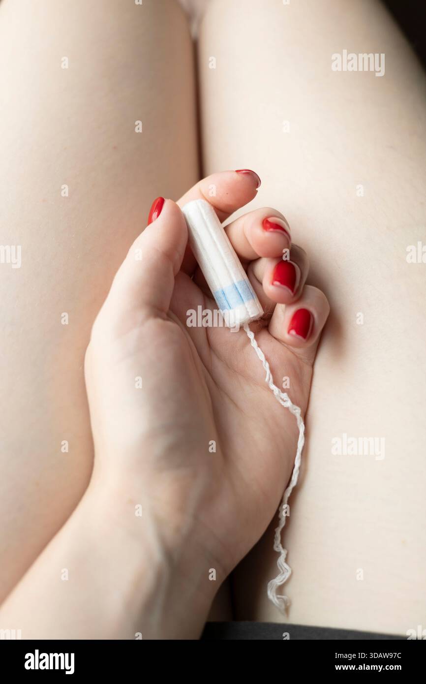 Une image en gros plan de la main d'une femme tenant un tampon blanc, avec des ongles rouge vif, symbolisant les soins menstruels, l'hygiène et la santé féminine Banque D'Images
