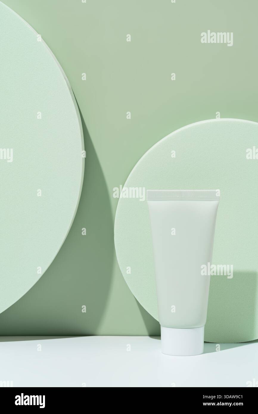 Design minimaliste mettant en valeur un tube cosmétique vert sur des podiums circulaires vert pastel. Les ombres douces et l'arrière-plan vert doux améliorent le produit. » Banque D'Images