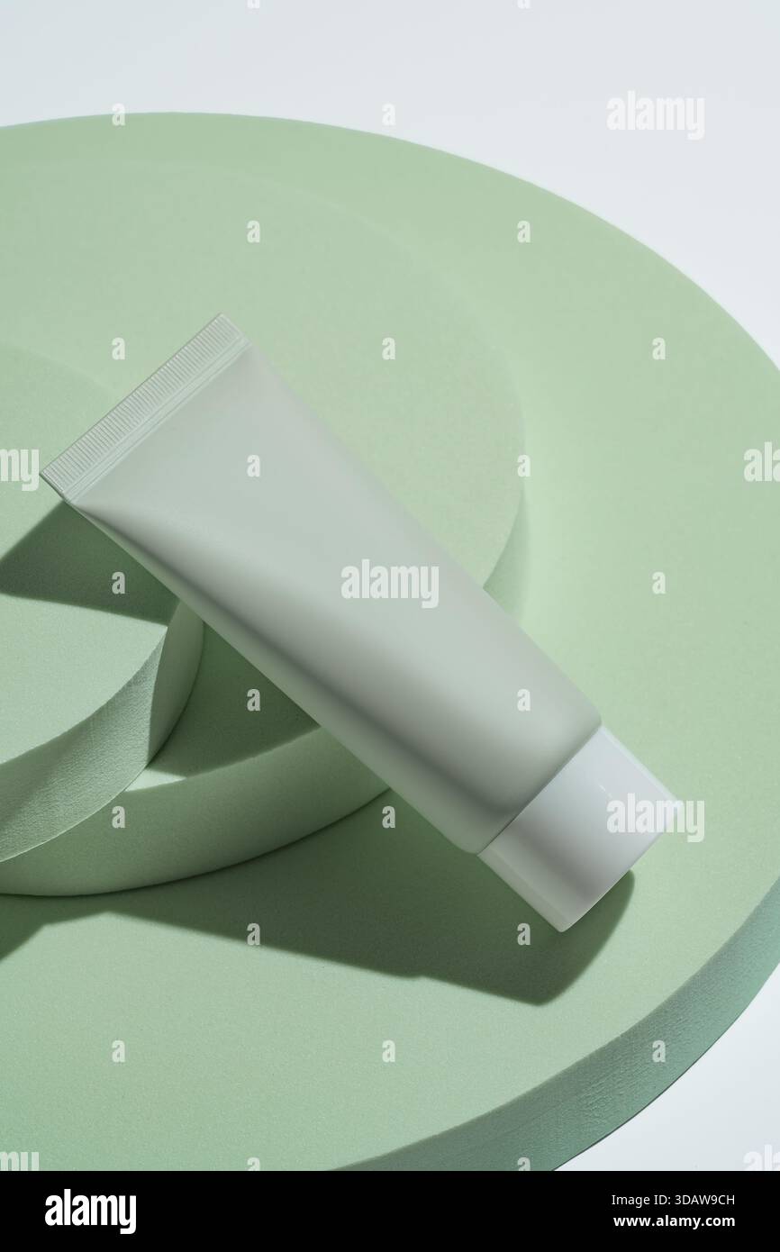 D'en haut, un tube cosmétique vert doux se trouve élégamment sur des podiums verts circulaires. La composition équilibrée met en évidence le design minimaliste par rapport au Banque D'Images