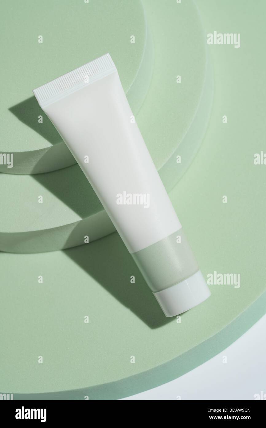 D'en haut, un tube cosmétique blanc est affiché sur des podiums verts circulaires qui se chevauchent, créant une présentation élégante avec des jeux d'ombres et minimaliste Banque D'Images