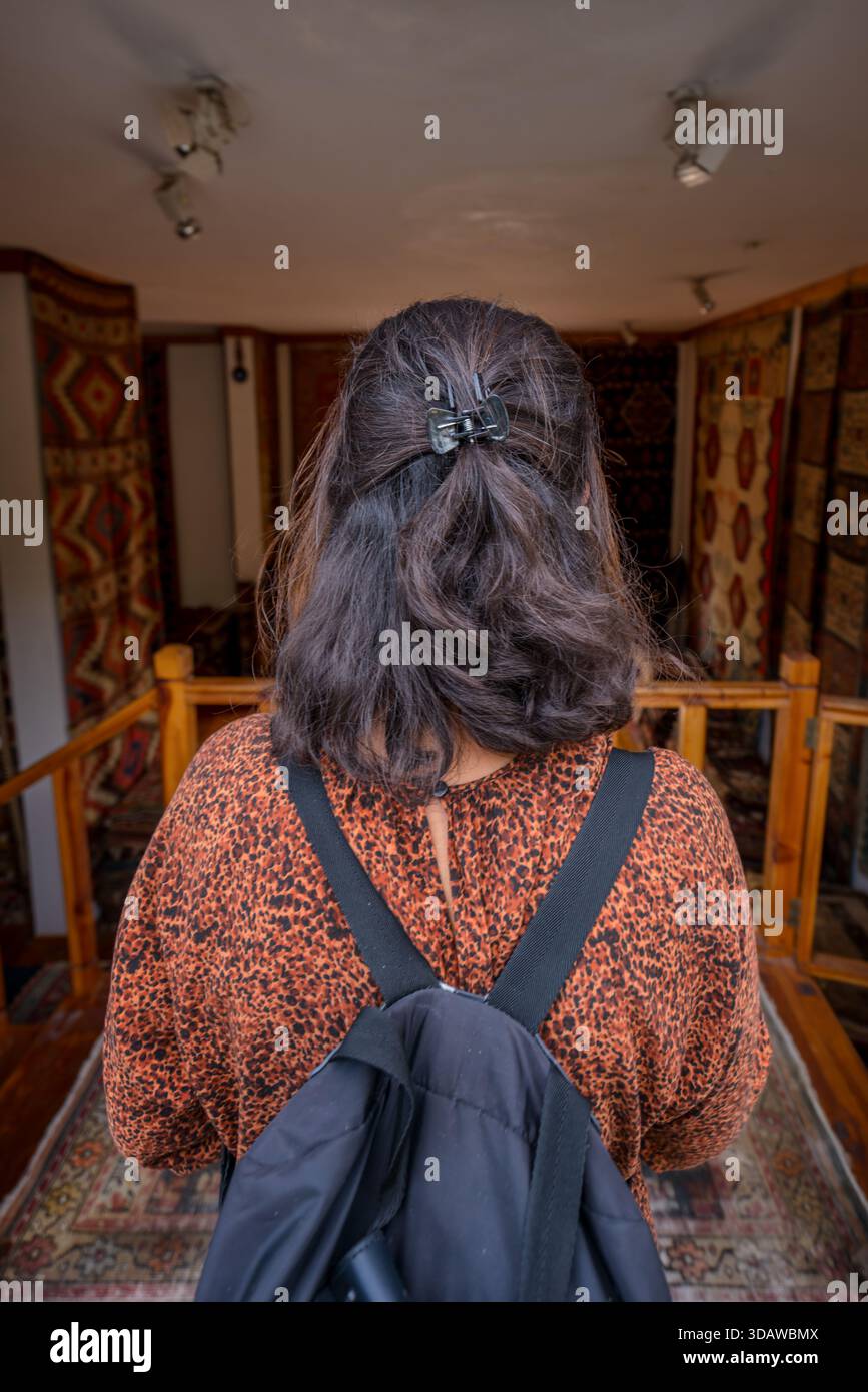 Une femme avec un sac à dos explore un magasin de tapis turc traditionnel, entouré de tapis vibrants et complexes sur l'affichage, créant un confortable et c Banque D'Images