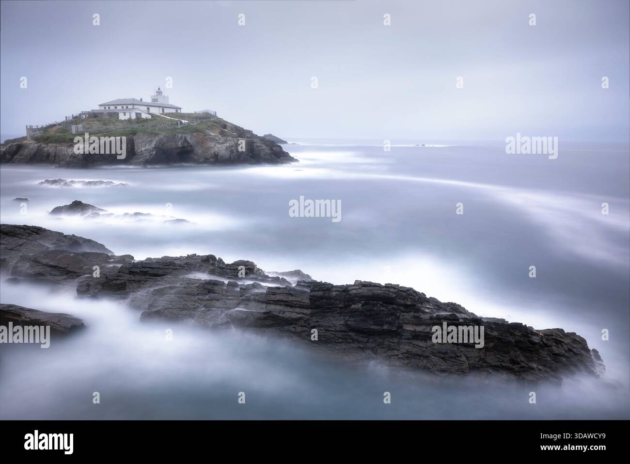 Vue captivante du phare d'Isla Pancha à Lugo avec des vagues éthérées s'écrasant contre la côte accidentée sous un ciel brumeux de l'aube, créant un calme et Banque D'Images