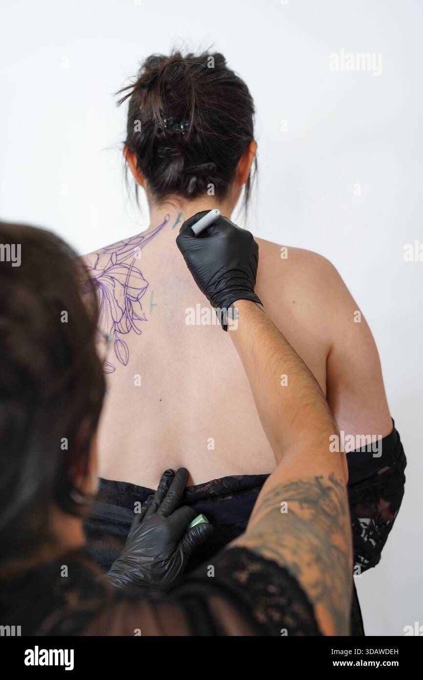 Un tatoueur féminin talentueux crée habilement un design personnalisé sur le dos d'un client. La session met en valeur l'art, la précision et la beauté O. Banque D'Images