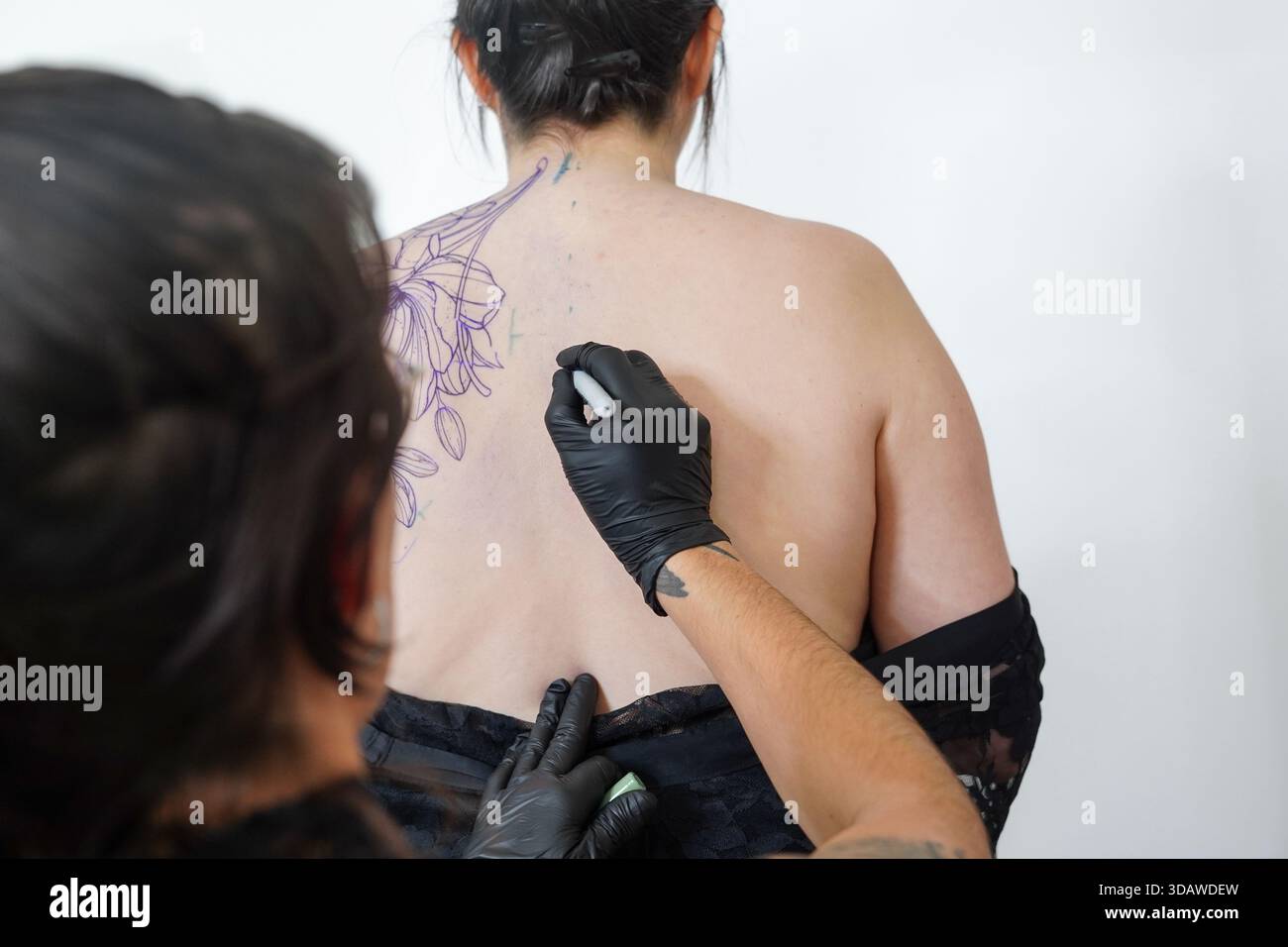 Une tatoueuse féminine en gants noirs dessine méticuleusement un dessin sur le dos d'un client lors d'une séance de tatouage. La séance de tatouage met en valeur la créativité Banque D'Images