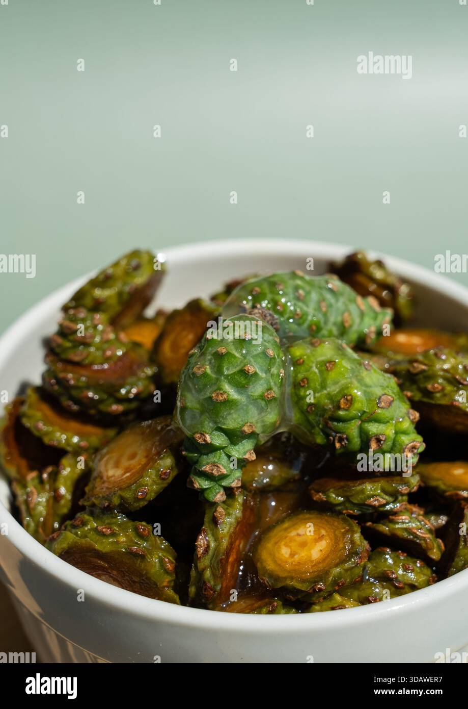 Un bol de miel de pommes de pin bio avec des pommes de pin vertes immergées dans du sirop, sur un fond vert doux. Le bol en céramique améliore le naturel Banque D'Images