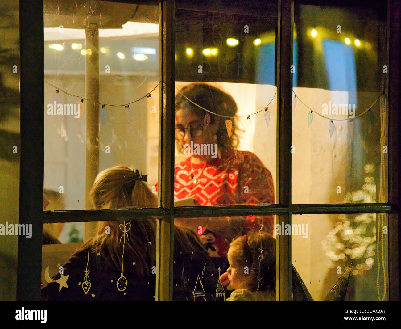 Un aperçu à travers une fenêtre festive et décorée d'une serveuse prenant une commande familiale dans un restaurant à Noël. Prise à Bourton sur l'eau. Banque D'Images