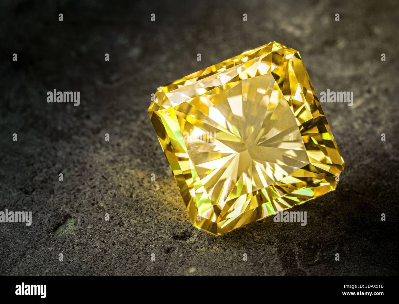 Un diamant jaune est assis sur une surface grise. Le diamant est taillé dans une forme carrée et est le centre de l'attention Banque D'Images