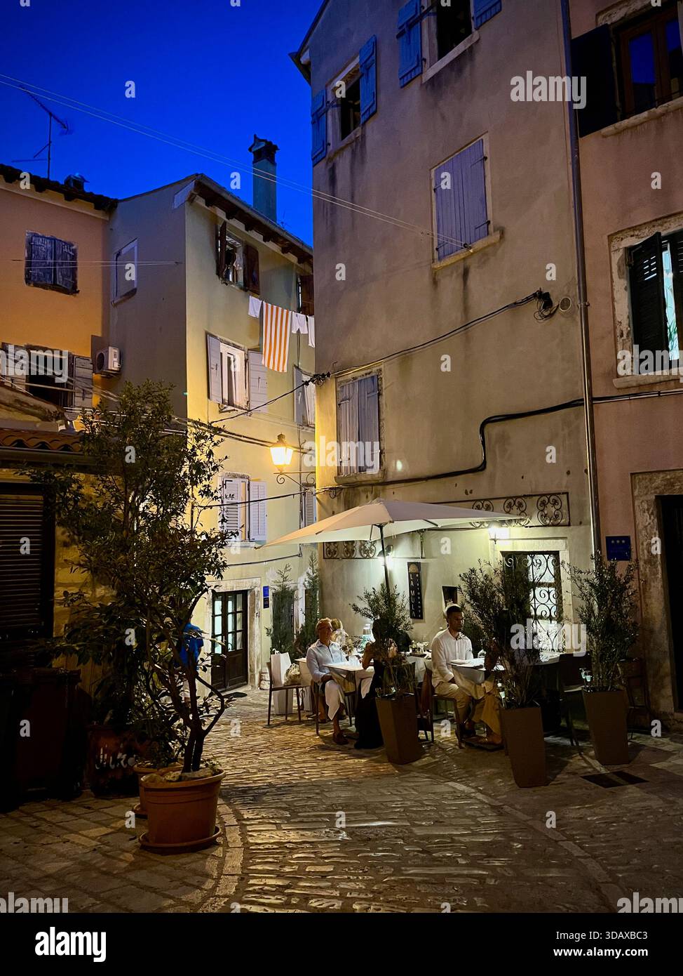 Une soirée intime se déroule dans une rue Rovinj éclairée par des lanternes, où le temps ralentit autour du dîner - Image de stock capturée avec un smartphone