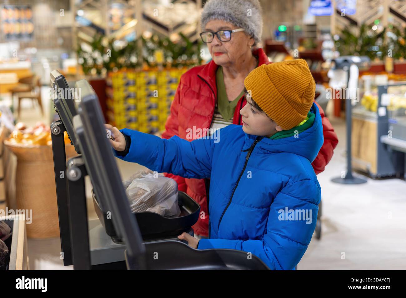 Petit-fils apprenant à sa grand-mère à utiliser la balance libre-service numérique à l'épicerie. Gen Alpha aide un baby-boom, la culture numérique Banque D'Images