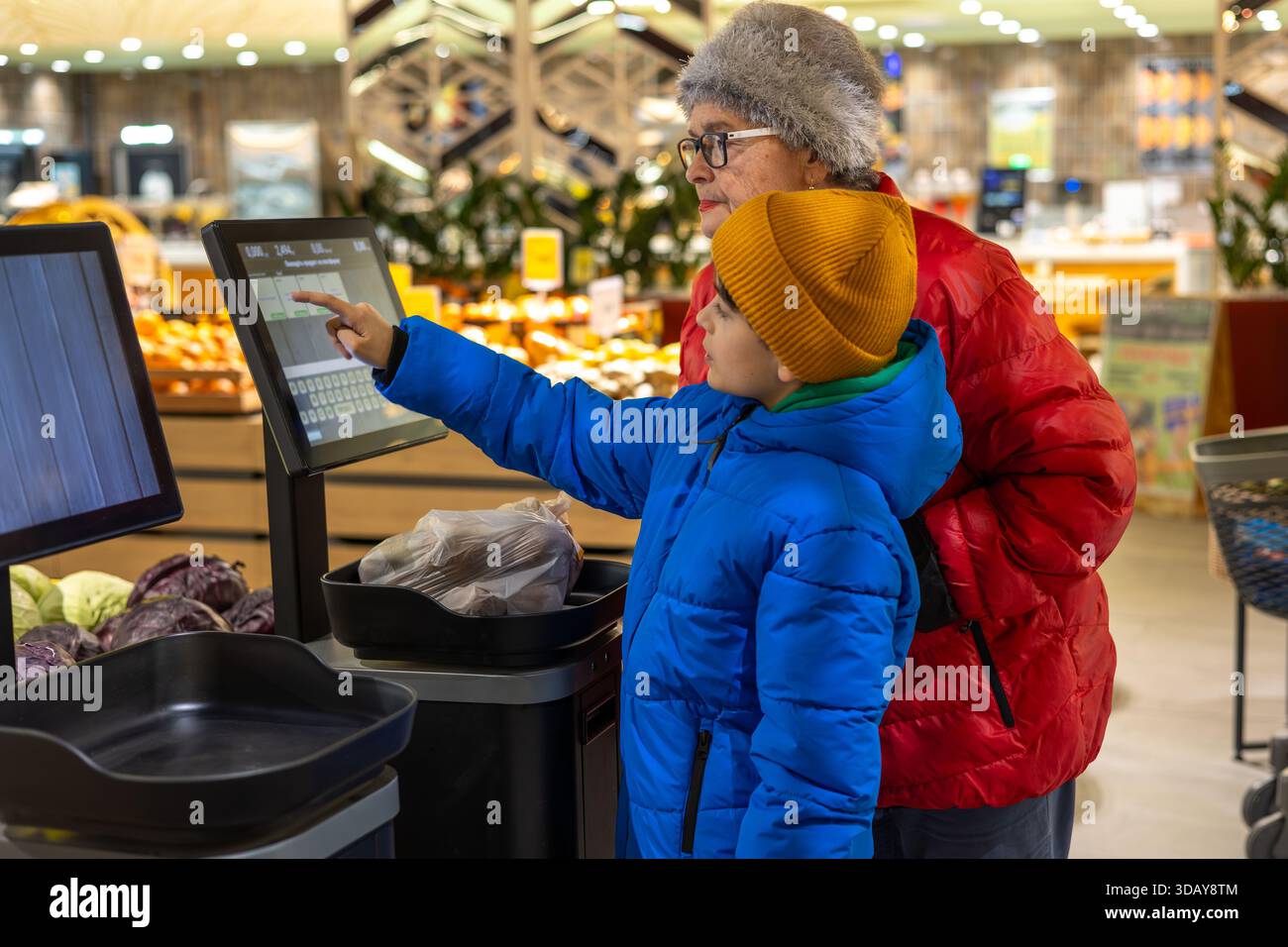 Petit-fils apprenant à sa grand-mère à utiliser la balance libre-service numérique à l'épicerie. Gen Alpha aide un baby-boom, la culture numérique Banque D'Images