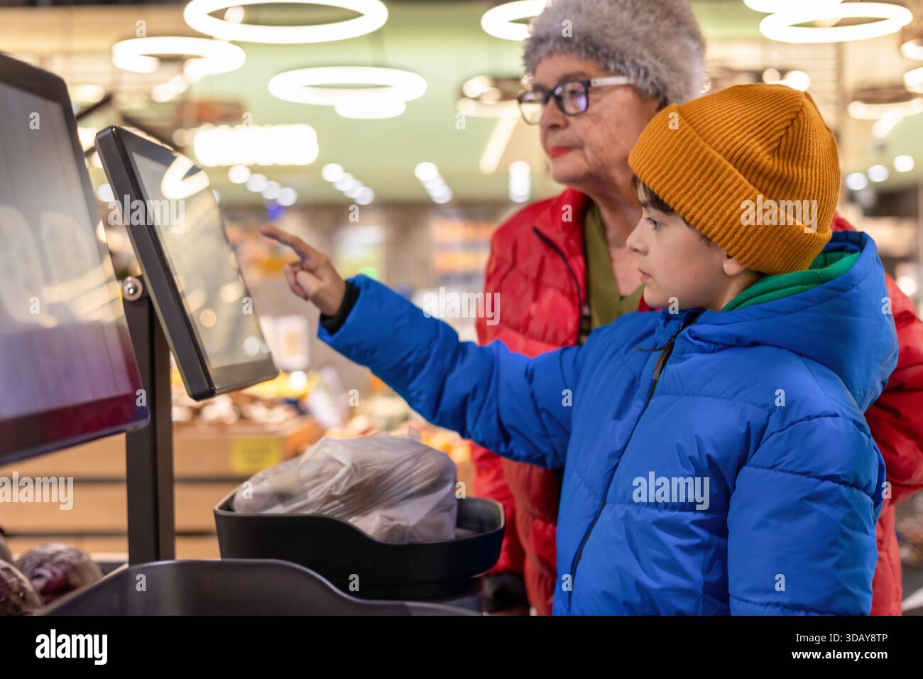 Petit-fils apprenant à sa grand-mère à utiliser la balance libre-service numérique à l'épicerie. Gen Alpha aide un baby-boom, la culture numérique Banque D'Images