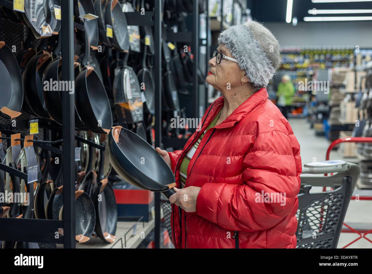 Femme âgée choisissant la poêle à frire dans la section des articles ménagers du supermarché – magasinage indépendant et mode de vie senior actif. mode de vie actif des seniors Banque D'Images