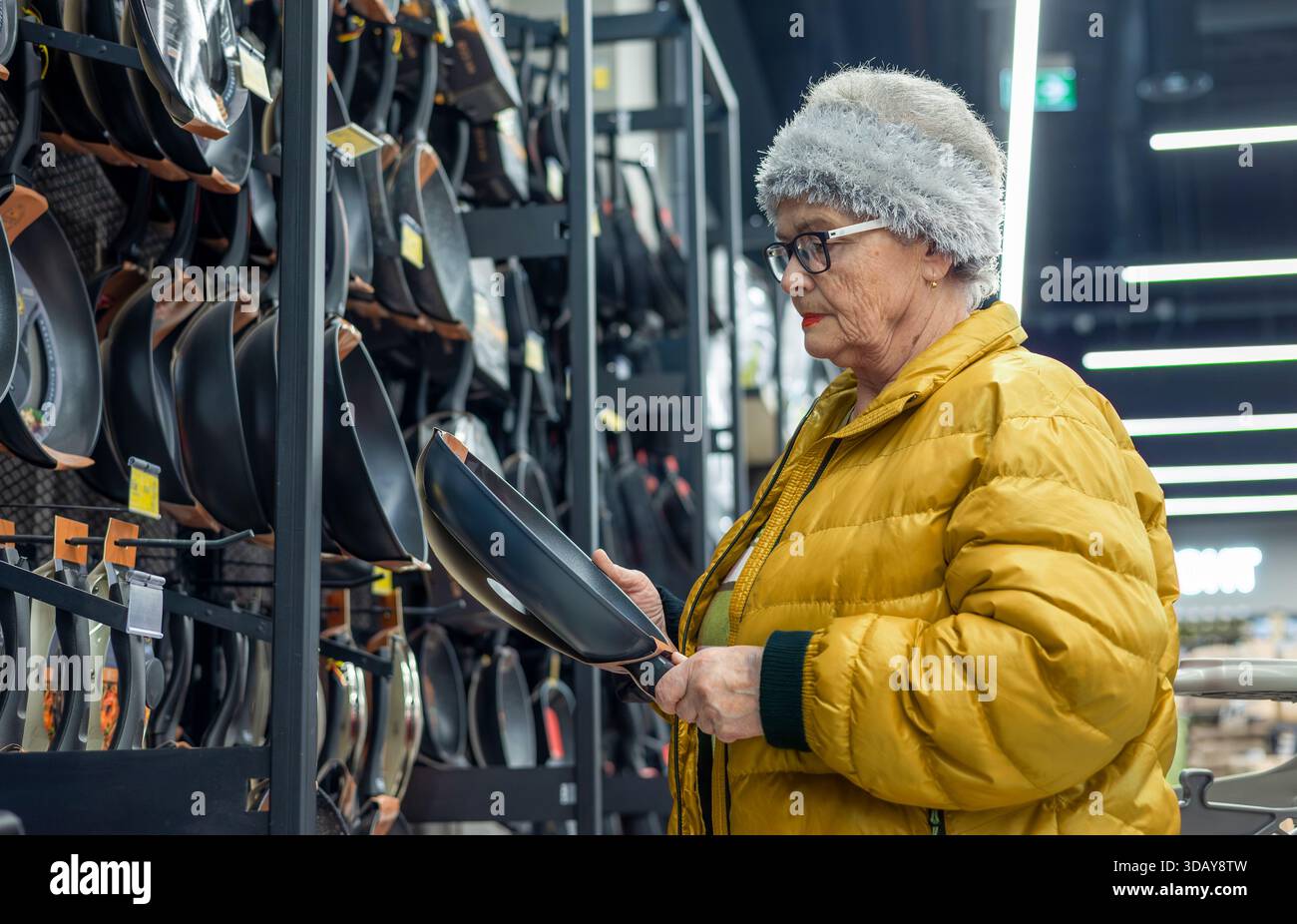 Femme âgée choisissant la poêle à frire dans la section des articles ménagers du supermarché – magasinage indépendant et mode de vie senior actif. mode de vie actif des seniors Banque D'Images