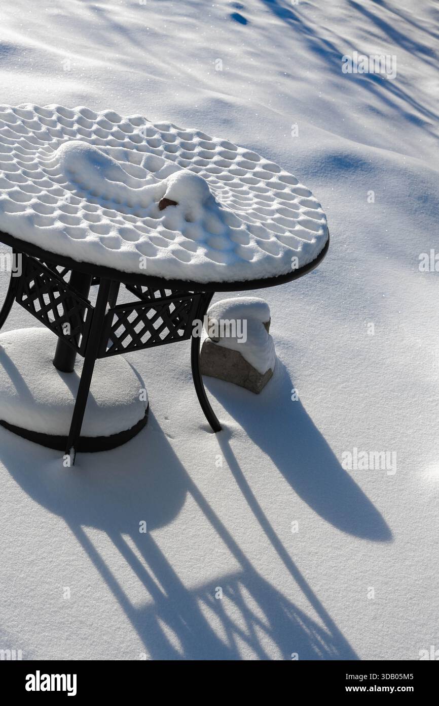 La lumière du soleil scintille sur une table de pique-nique en métal recouverte de neige, créant des motifs étonnants dans l'étreinte hivernale à Ludington, Michigan. Banque D'Images