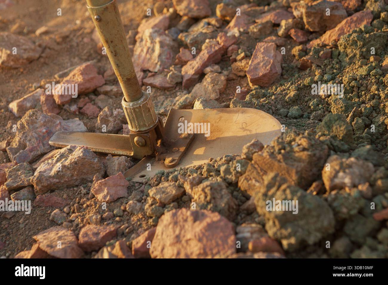 Une pelle militaire rouillée creuse dans la terre rocheuse brun-rougeâtre, montrant une variété géologique, suggérant des fouilles ou des explorations. Banque D'Images