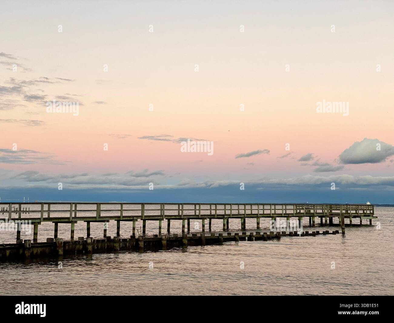 Jetée en bois s'étendant au-dessus de l'eau calme au coucher du soleil sous un ciel de couleur pastel - Image de stock capturée avec un smartphone