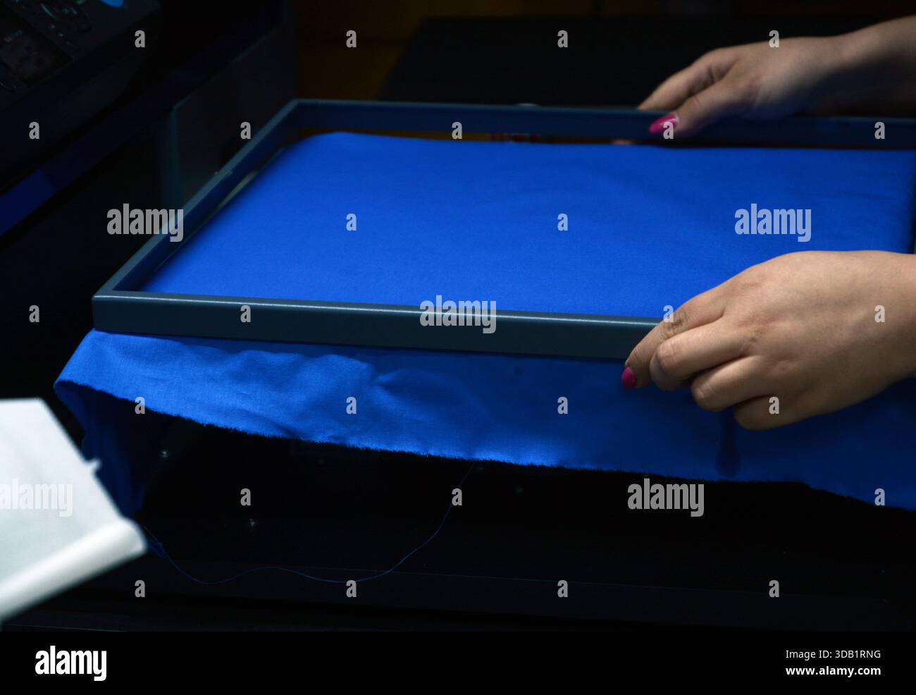 préparer la toile bleue pour l'impression avec le cadre en métal lourd dans la machine d'impression numérique et les mains de travailleuse de femme le font très habile Banque D'Images