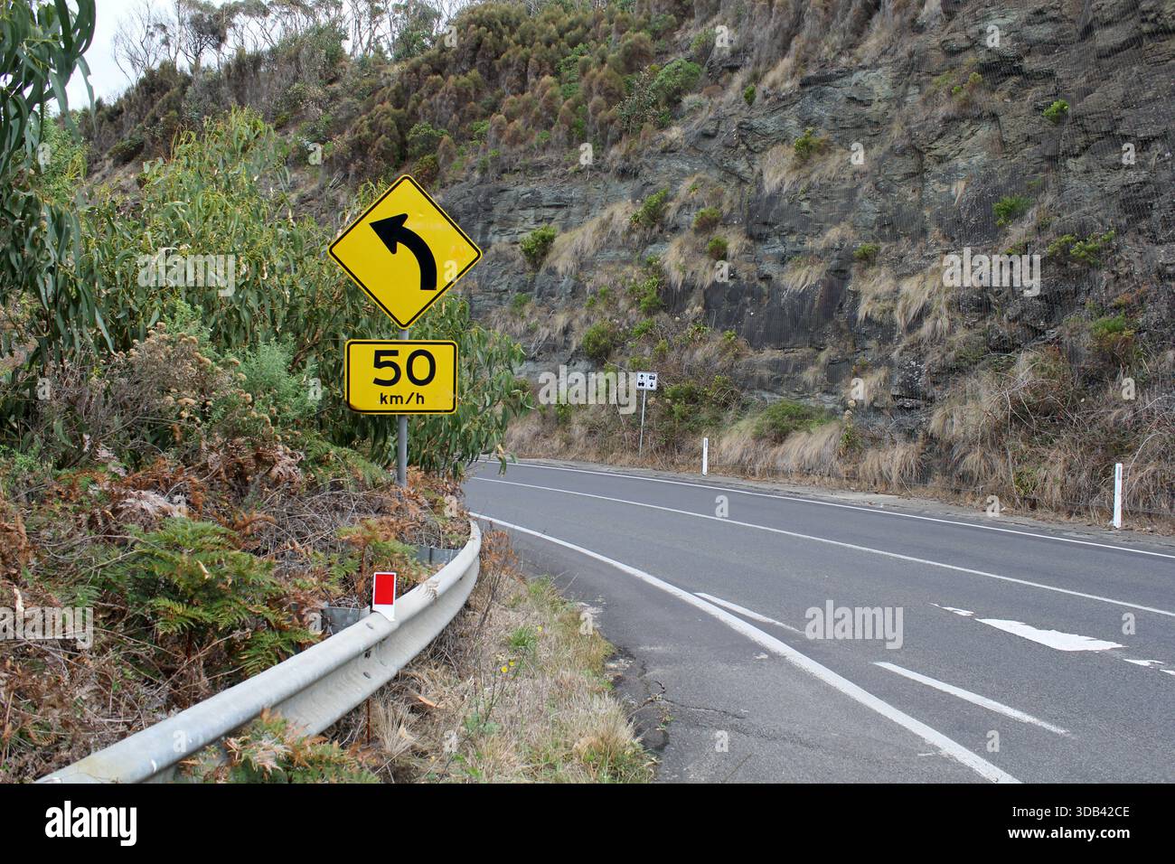 Great Ocean Road avec panneau de limitation de vitesse serpentant à travers une montagne dans le Victoria, Australie Banque D'Images