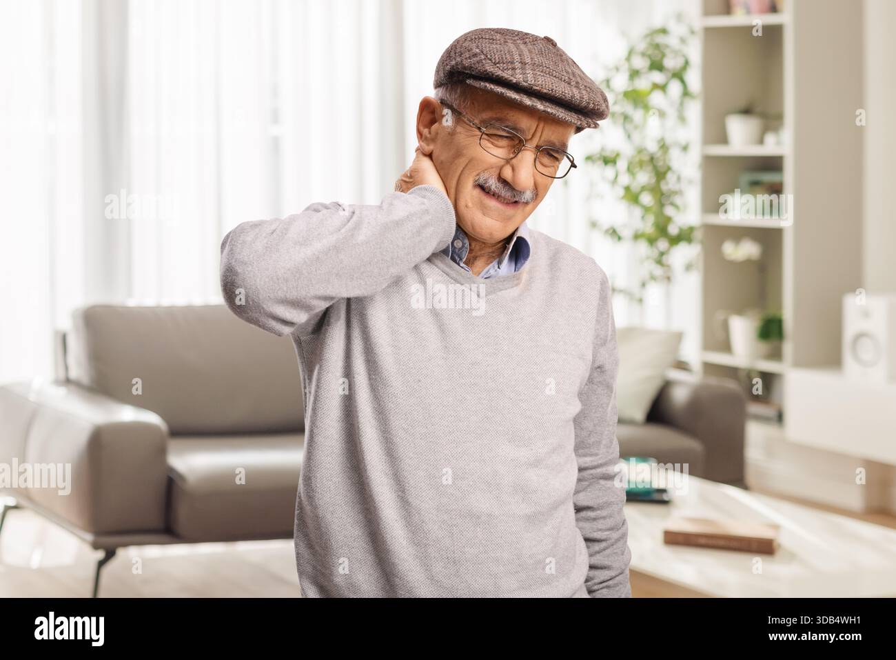 Homme âgé avec le cou raide debout dans un salon Banque D'Images