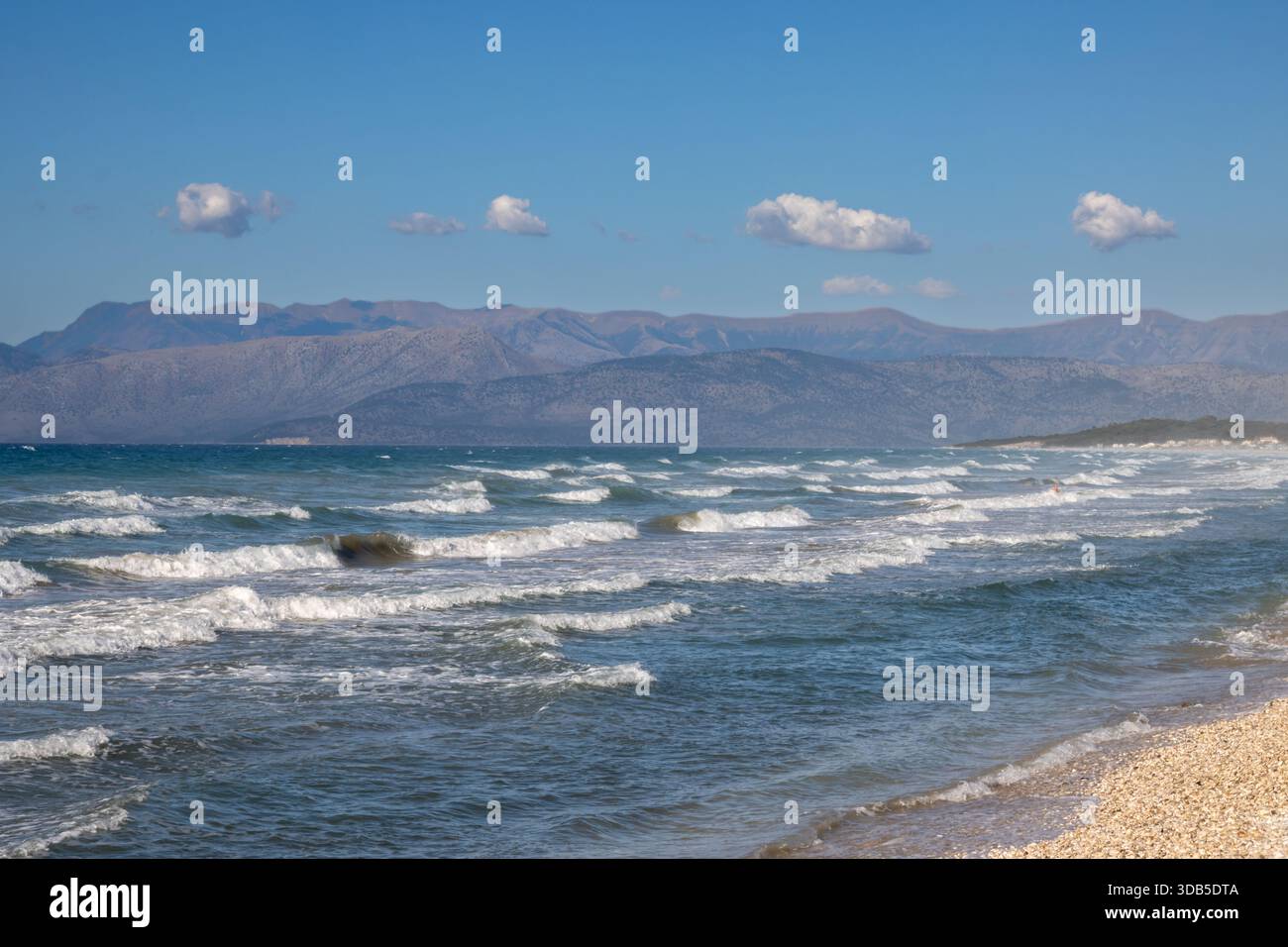 Mer Ionienne avec des vagues spectaculaires pendant une journée d'été tardive. Montagnes albanaises en arrière-plan. Ciel bleu avec des nuages blancs. Nord de l'île Corfou ( Banque D'Images