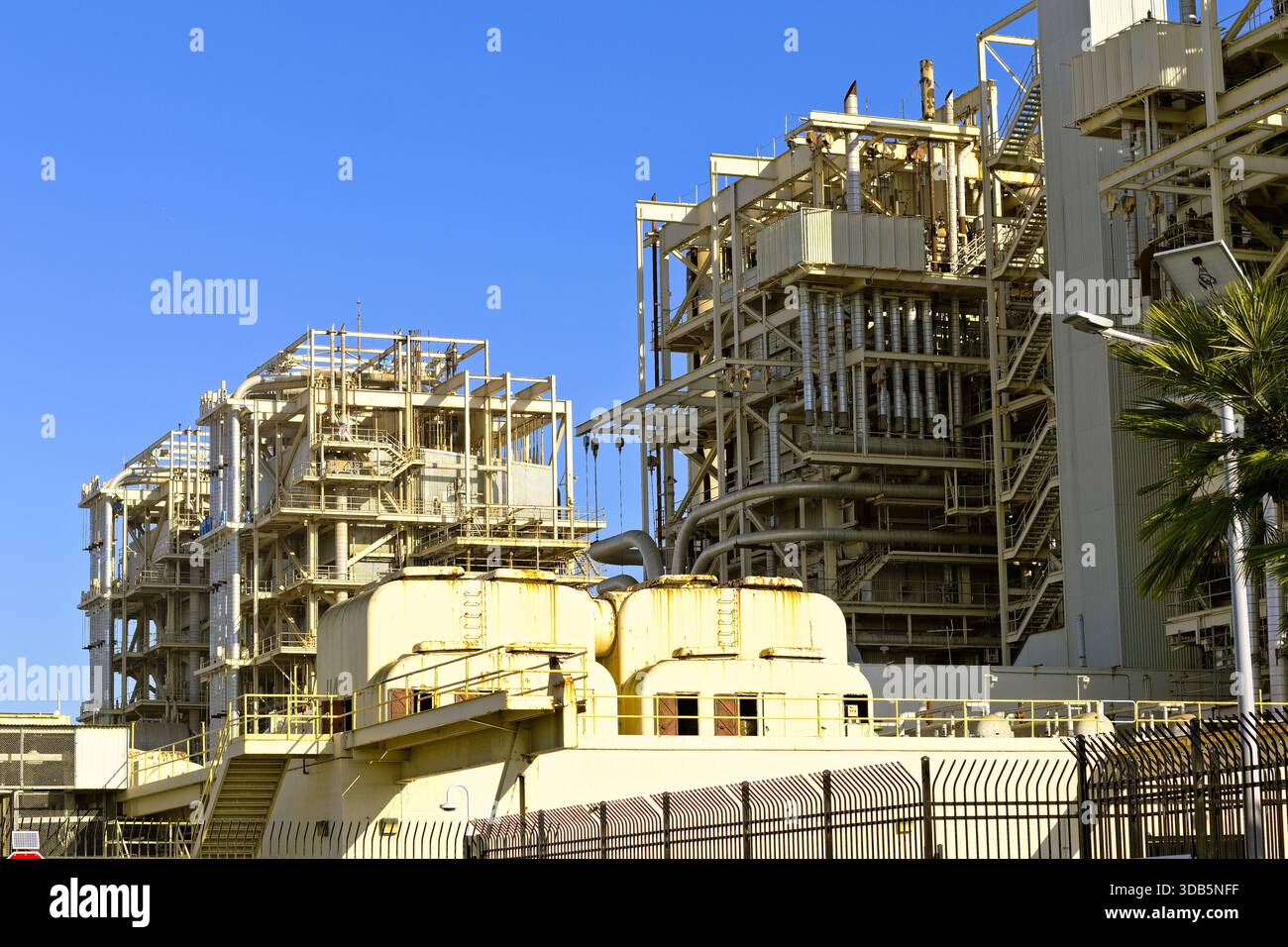 Grande centrale électrique et complexe industriel avec ossature en acier, tuyaux et périmètre clôturé sous ciel bleu clair, représentant l'infrastructure énergétique. Banque D'Images