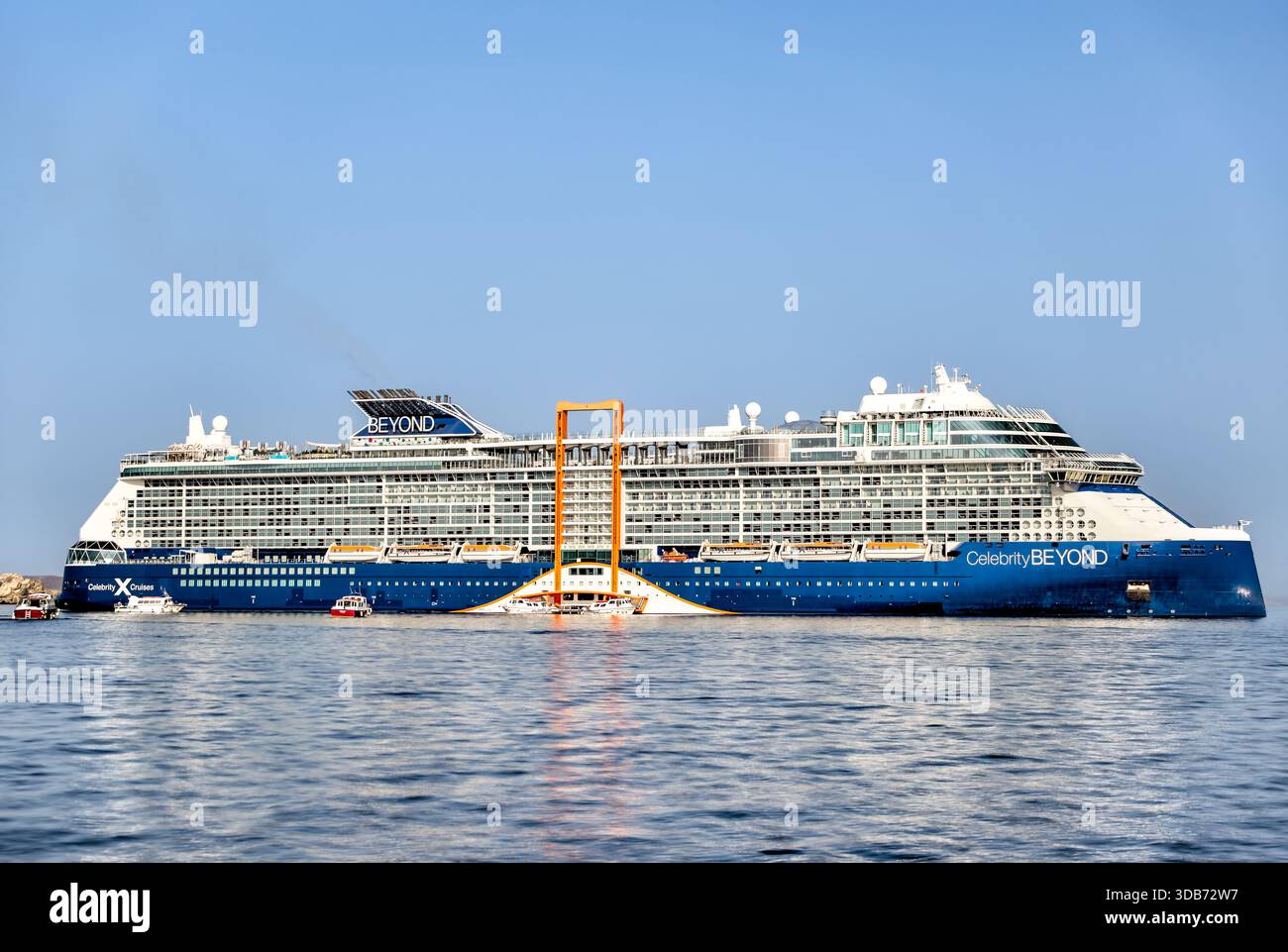 Celebrity Beyond bateau de croisière amarré près de la ville de Mykonos avec des bâtiments à flanc de colline en arrière-plan, Grèce. Banque D'Images