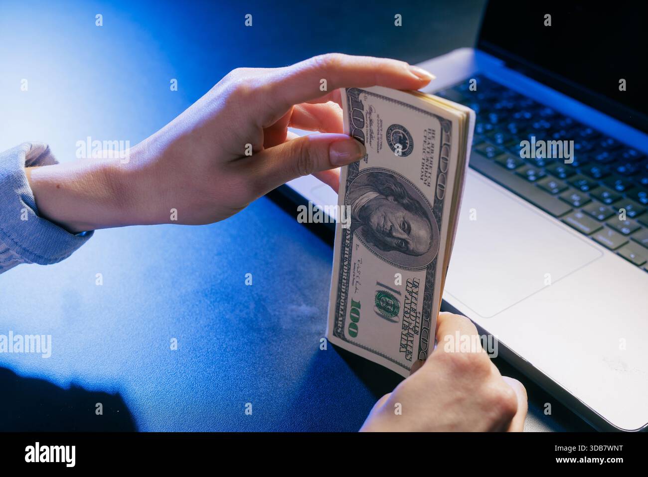 Mains tenant une pile de dollars américains près d'un ordinateur portable, symbolisant les gains en ligne, la finance numérique ou les transactions commerciales sur Internet Banque D'Images