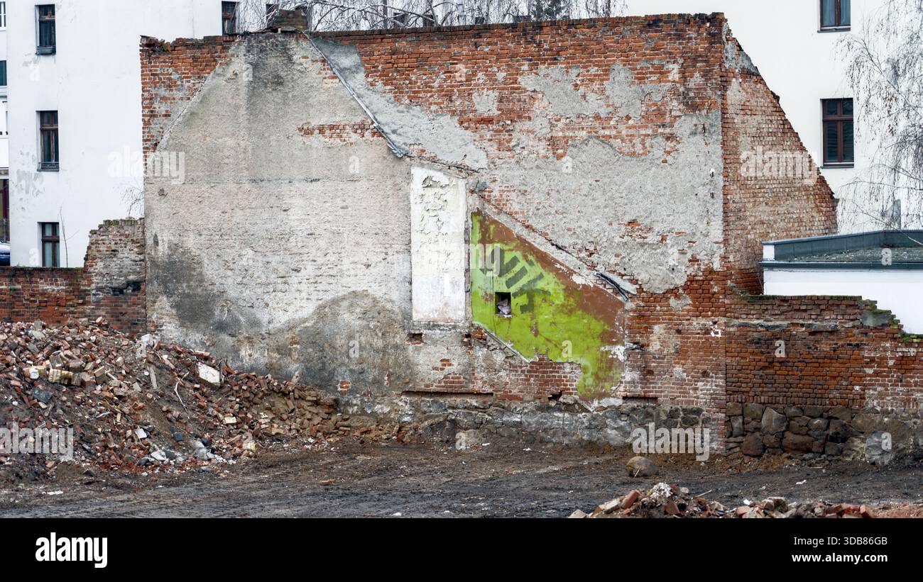 Un mur de briques en décomposition recouvert de graffitis se dresse sur un site de démolition, entouré de gravats dans un environnement urbain. Banque D'Images